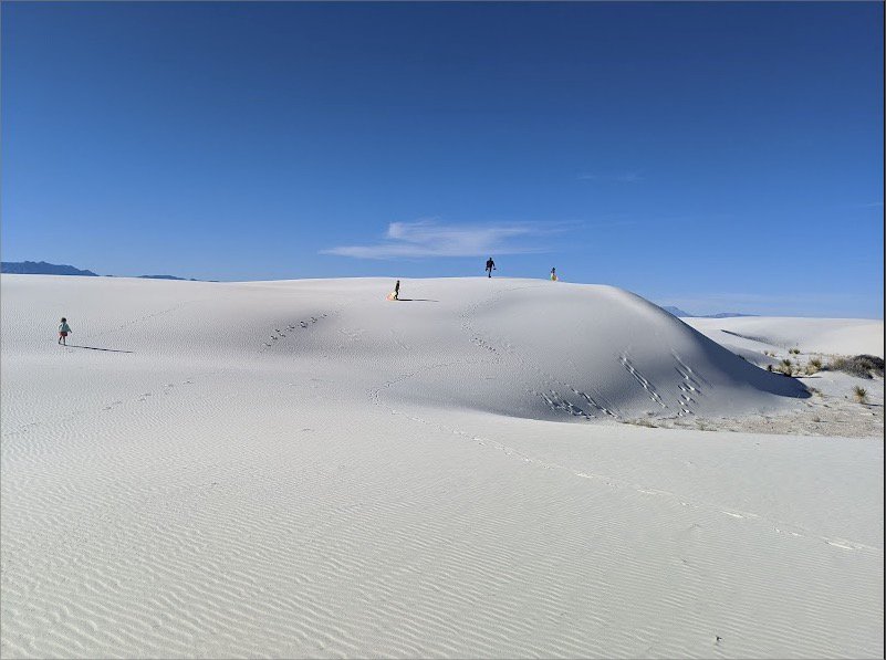 A group of people on a snow covered hill with White Sands National Monument in the background.